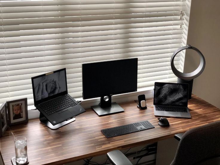A modern wooden desk featuring multiple laptops, a central monitor, and keyboard.